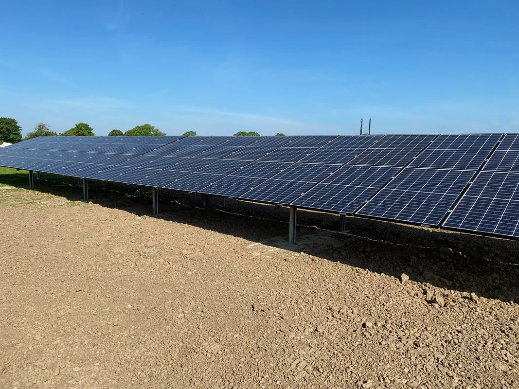 Ground-mounted solar PV panels on steel supports beneath a blue sky