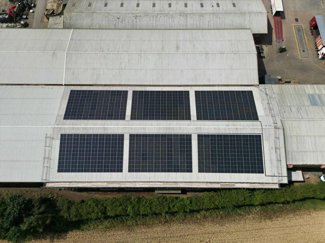 Aerial view of two rows of solar PV panels on a large agricultural building roof